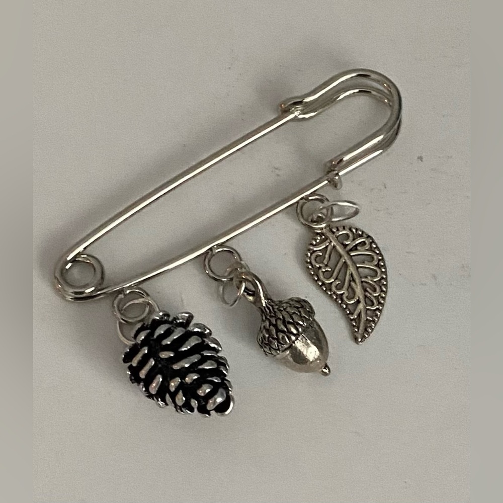 Nature charms safety pin brooch with pine cone, acorn, and leaf charms.